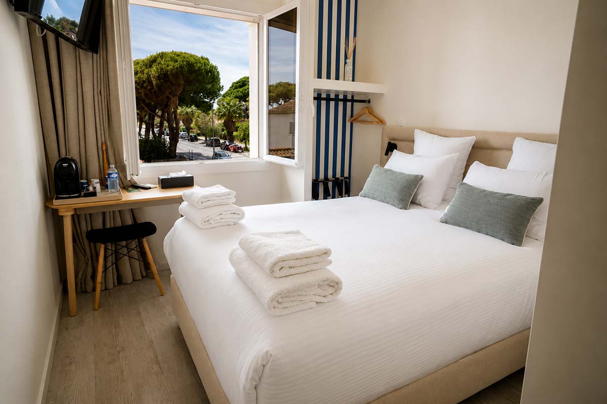 Chambre Double Classique avec vue sur les pins — Hôtel Le Kallisté à Hyères L’Ayguade Chambre double classique lumineuse de l’Hôtel Le Kallisté à Hyères L’Ayguade avec lit double, fenêtre ouverte et vue sur les pins méditerranéens